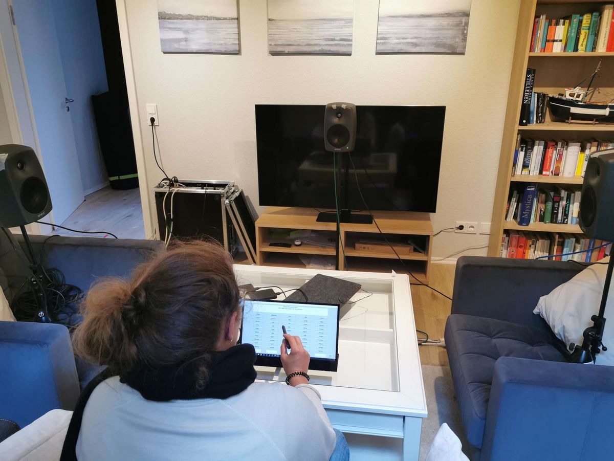 Fünf nasse Sessel oder eine graue Couch? — Julia Schütze — Auch wenn es auf den ersten Blick aussehen mag, wie ein Versuchsaufbau zu Hause, ist auf dem Bild ein Versuchsaufbau im neuen Living Room Lab im W02 zu sehen. Das Labor sieht aus wie das typisch deutsche Wohnzimmer, mit grauem Sofa, Couchtisch, Orchideen und Fotos. Auf dem Bild sieht man einen Versuchsaufbau zur Untersuchung der Sprachverständlichkeit in einer alltagsnahen Umgebung - hier dem Living Room Lab. 