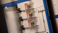Three identical looking modules are mounted vertically on a grey plate and connected with small pipes and connectors. 