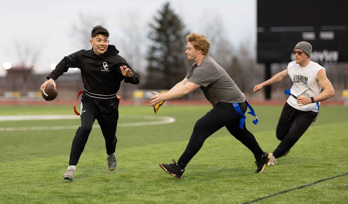Flag Football Studierende spielen Flag Football auf einem Rasenplatz. Ein Spieler rennt mit dem Ball, andere versuchen ihn abzufangen.