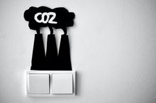 Über zwei weißen Lichtschaltern sind mit schwarzer Pappe drei Schornsteine aufgeklebt, aus denen eine Wolke kommt. In dieser Wolke steht in weißer Schrift CO2.