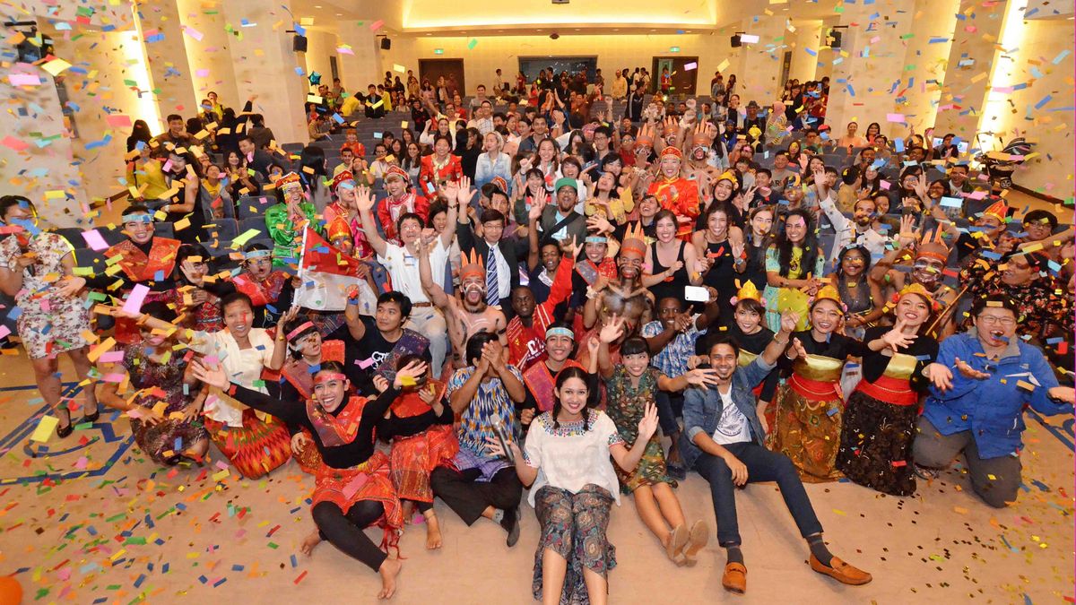 Das Bild zeigt eine große Gruppe von Studierenden, Mitarbeitenden und möglicherweise Absolvent*innen der National Dong Hwa University (NDHU), die in einem Auditorium oder einer großen Halle eine Feier veranstalten. Konfetti fliegt durch die Luft, und die Menschen lächeln, jubeln und machen Fotos. Viele tragen festliche Kleidung und Hüte, was auf einen besonderen Anlass wie eine Abschlussfeier oder ein kulturelles Fest hindeutet. Die Szene vermittelt eine fröhliche und ausgelassene Atmosphäre.