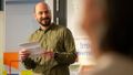 The picture shows Matheus Silveira Mendes. He is holding a piece of paper in his hand while giving a speech. He smiles at the audience.