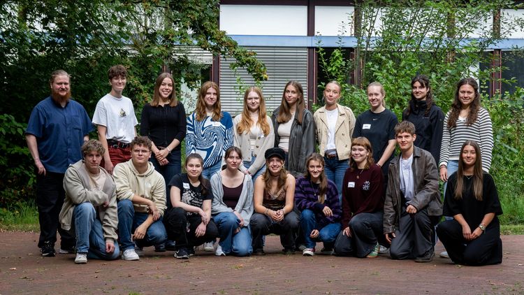 Das Bild zeigt 19 der 22 Freiwilligen, die sich zu einem Gruppenbild aufgestellt haben. Sie stehen vor einem Unigebäude und lächeln in die Kamera.