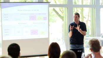 UniTalk Eine Person hält einen Vortrag mithilfe einer Präsentation vor mehreren Zuschauenden.