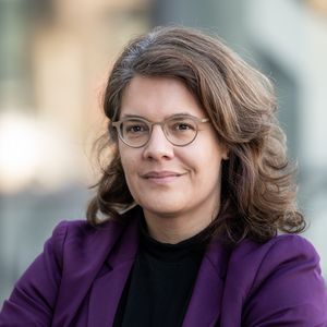 Porträt von Prof. Dr. Sina Farzin, die einen lila Blazer und ein schwarzes Oberteil trägt. Sie trägt Brille und hat braunes, schulterlanges, gelocktes Haar. Sie lächelt leicht mit geschlossenem Mund. 