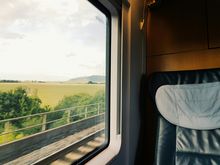 Das Bild zeigt einen Ausschnitt von einem Sitzplatz in einem ICE der Deutschen Bahn. Auf der linken Hälfte ist der Blick aus dem Fenster und rechts sieht man den oberen Teil des Sizplatzes.
