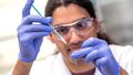 A scientist has a narrow pipette in his hand with which he places a hair-thin wire in the printing nozzle made of glass. 