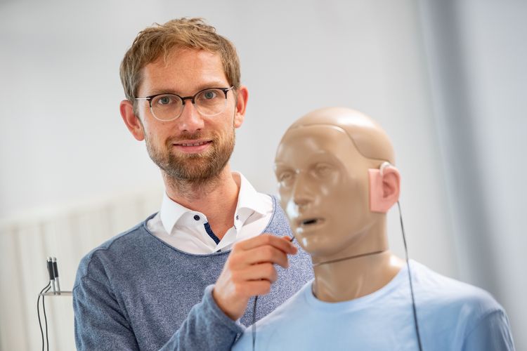 Kai Siedenburg mit einer lebensgroßen Modellpuppe, die Hörgeräte trägt.
