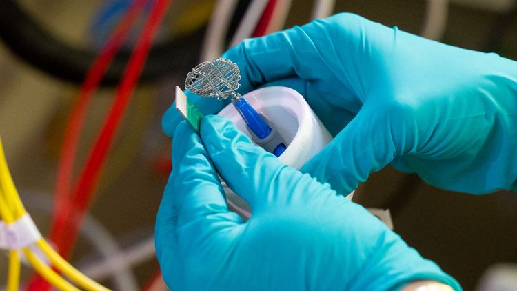 Close-up of two hands in blue gloves holding a device with two electrodes. 