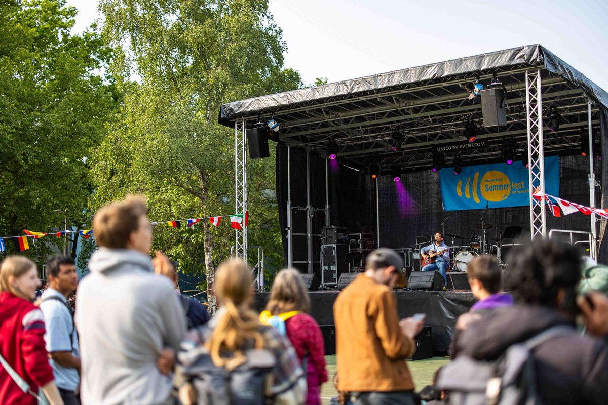 Personen, die vor der Bühne versammelt sind. Eine Person spielt hier auf einer Gitarre.