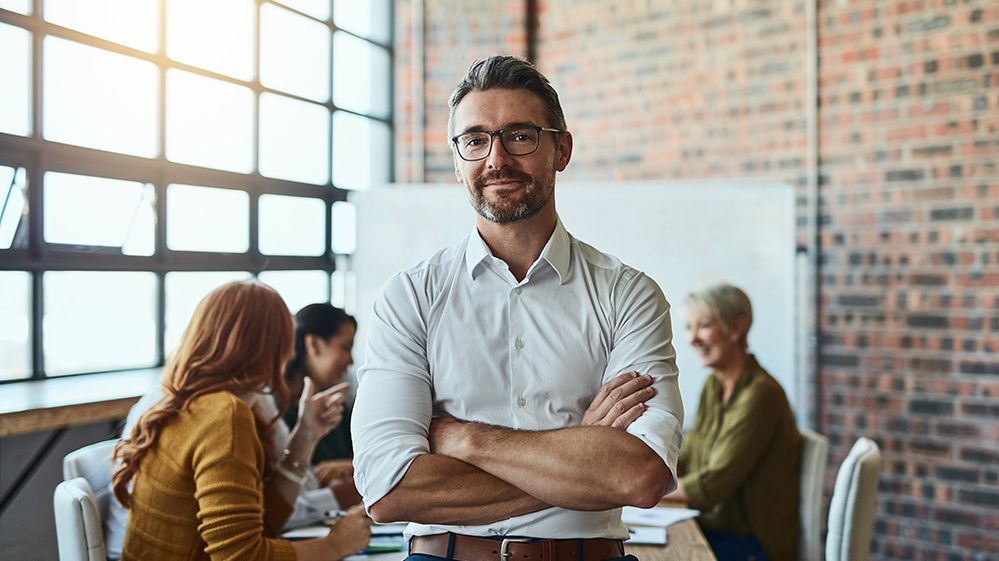 Wirtschaft und Recht  Auf dem Bild ist ein Mann im Büro zu erkennen. Im Hintergrund sind weitere Kolleginnen und Kollegen in einer Besprechung.