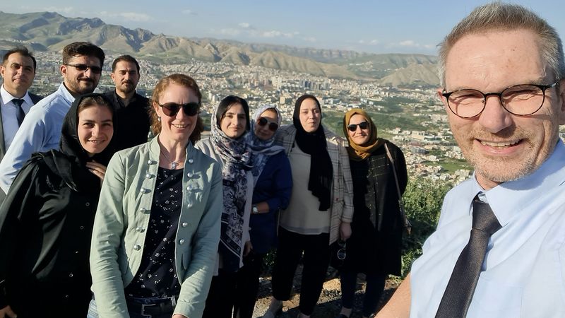 Das Bild zeigt Clemens Hillenbrand und neun weitere Projektteilnehmende. Im Hintergrund sind eine Stadt und Berge zu erkennen. Das Bild ist ein Selfie.