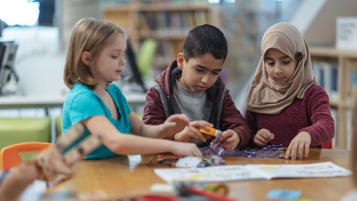 Drei Kinder im Grundschulalter sitzen nebeneinander an einem Tisch und basteln. 