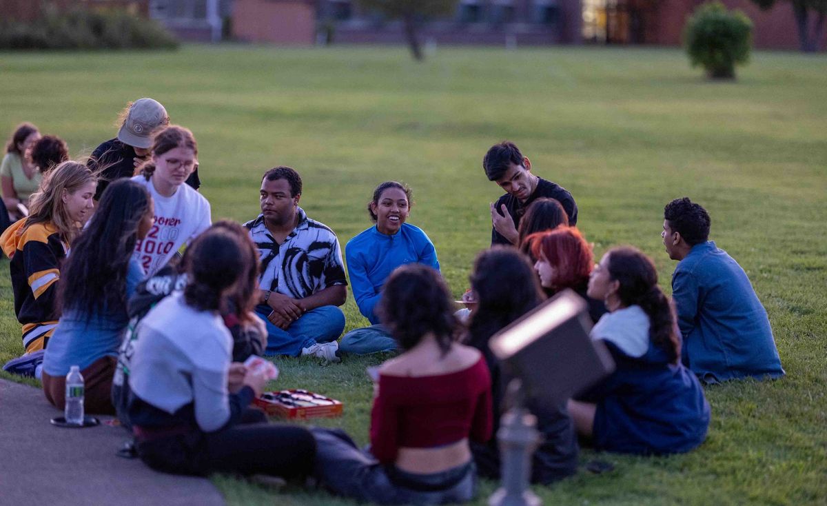 University of Wisconsin–Superior Eine Gruppe Studierenden sitzt im Kreis auf dem Rasen, einige spielen Karten.
