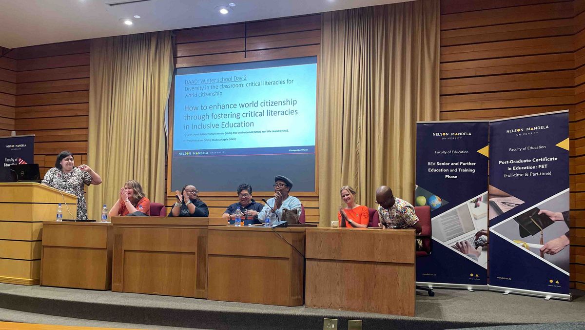 DAAD Winter School 2023 in South Africa A podium discussion or presentation in a lecture hall. Several people sit behind a podium, one person speaks into a microphone.