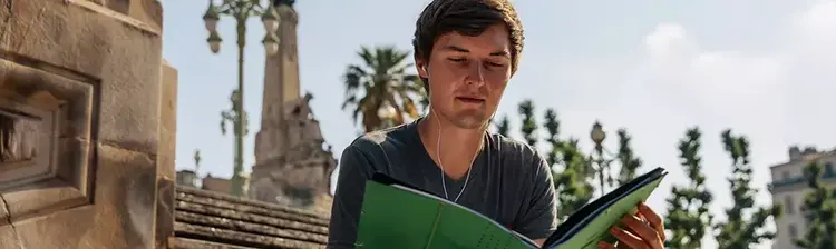 Studieren im Ausland Ein junger Mann liest auf einer steinernen Treppe vor historischen Gebäuden.