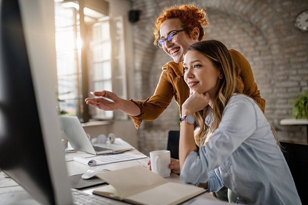 Online-Marketing Auf dem Bild sind zwei Frauen während einer Besprechung vor einem Computer zu sehen.