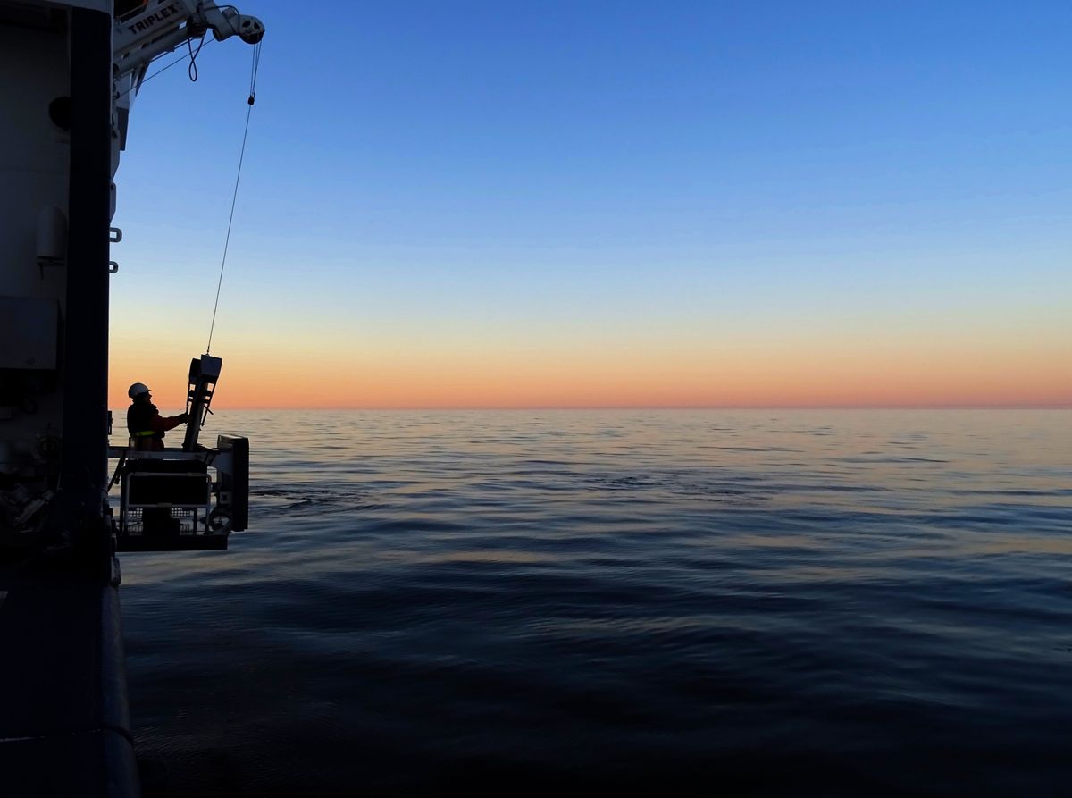Stille Wasser, tiefe Entdeckungen — Leonie Jaeger — In den letzten goldenen Sonnenstrahlen wird unser Sedimentprobennehmer ins ruhige Wasser der Ostsee gelassen. Als Studentin an Bord des Forschungsschiffs SVEA untersuche ich Methan und Metallkontaminationen im Sediment. Unser Ziel ist es, die alarmierende Verschmutzung und das Wachstum sauerstoffarmer Todeszonen besser zu verstehen. 