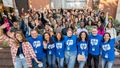 Group photo of the international students and the tutors on the campus of the University of Oldenburg. The tutors in the front row are wearing blue T-shirts. Behind them are several rows of students waving at the camera.