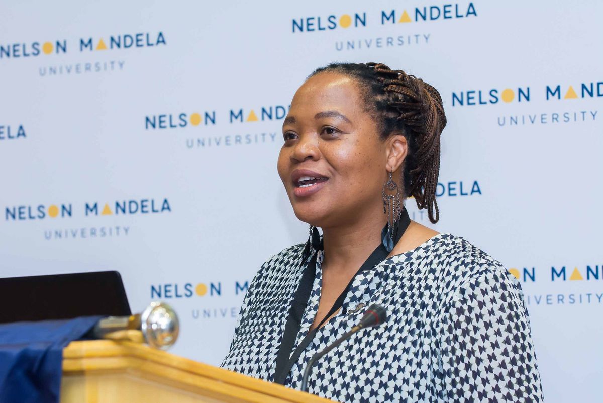Delegationsbesuch an der NMU Eine Frau spricht an einem Pult und steht vor einem Mikrofon. Sie spricht im Rahmen des Delegationsbesuchs an der Nelson Mandela University.