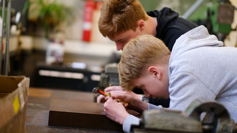 Zwei Jungs arbeiten in einer Werkstatt. Einer hält einen Hammer in der Hand.