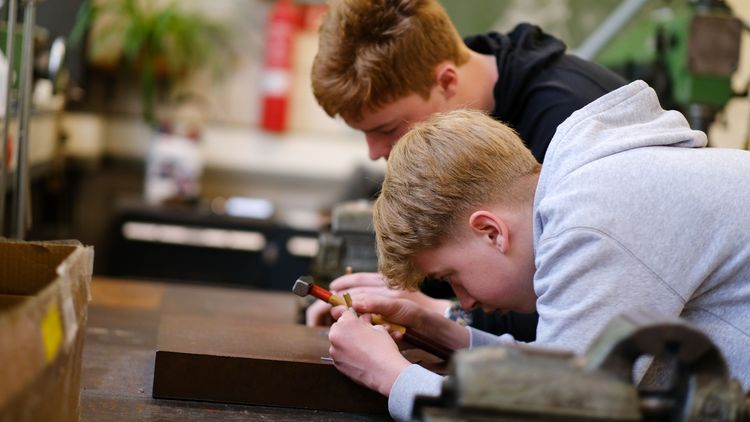 Zwei Jungs arbeiten in einer Werkstatt. Einer hält einen Hammer in der Hand.