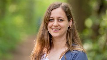 Portrait einer jungen Frau mit langen Haaren vor einem unscharfen, grünen Hintergrund.