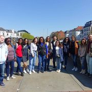 City tour A group of about 15 smiling people in front of a cityscape with red brick houses and a river.