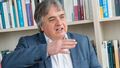 Portrait photo of the social scientist Martin Heidenreich in front of a wall of books.
