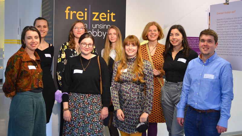 Die acht Studentinnen und ein Student vor einem Plakat ihrer Ausstellung.