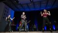 The picture shows the band SWAY at a performance. Three band members play wind instruments, one drums, two play guitar, one keyboard. Three others sing and dance.