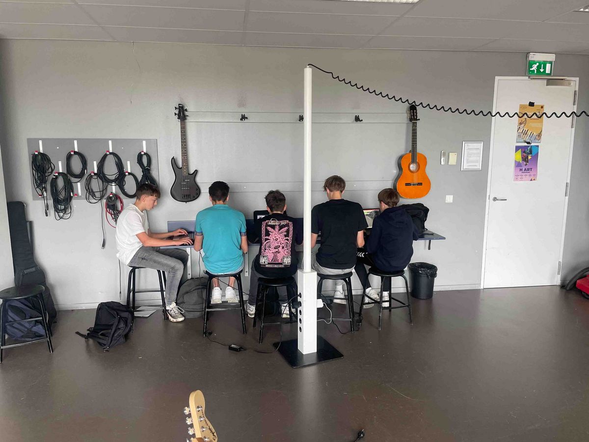 Teaching Across Borders Ein Raum in der Schule Stad&Esch, in dem fünf Schüler*innen an Notebooks sitzen und konzentriert arbeiten. Der Raum ist mit Gitarren und Kabeln ausgestattet.