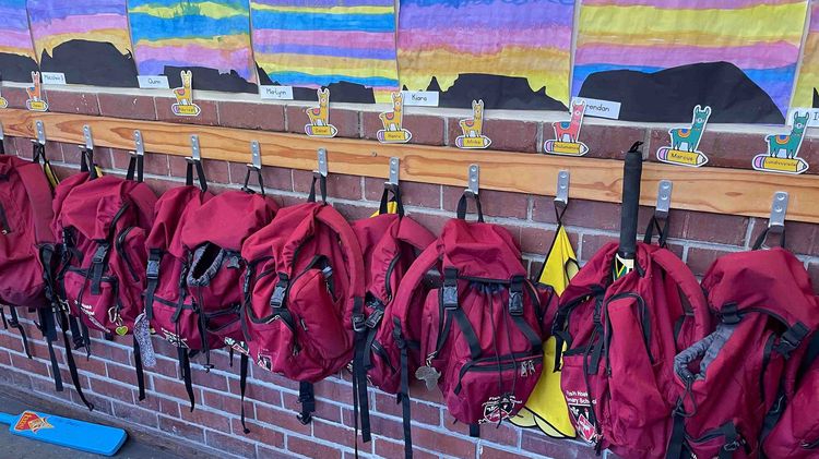 Internship abroad (school) A classroom or hallway in a school decorated with children's paintings of mountains and a sunset. Red school bags with llamas and children's names hang underneath.