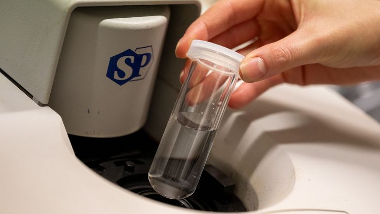 Close-up of a hand placing a glass tube in a machine.