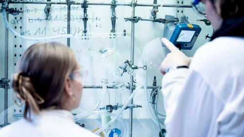 Two persons are seen from the back. They are looking at several chemical tubes and devices.
