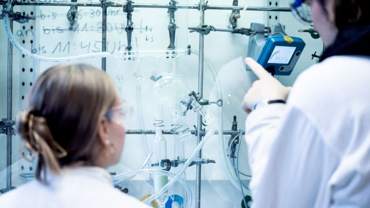 Two persons are seen from the back. They are looking at several chemical tubes and devices.