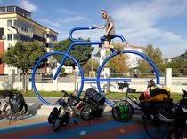 Grünes Reisen  Ein Mann sitzt auf einem großen, blauen Fahrrad-Kunstwerk in einer Stadt.