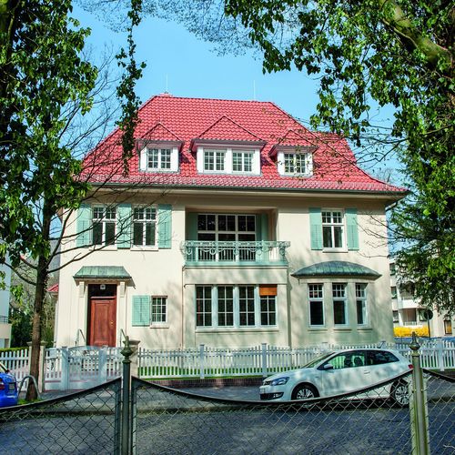 Das Bild zeigt das Karl-Jaspers-Haus im Dobbenviertel. Das Haus ist eine zweistöckige Villa mit rotem Dach und gelbem Anstrich. Vor dem Haus parkt ein Auto. Das Haus ist von einem weißen Zaun umgeben.