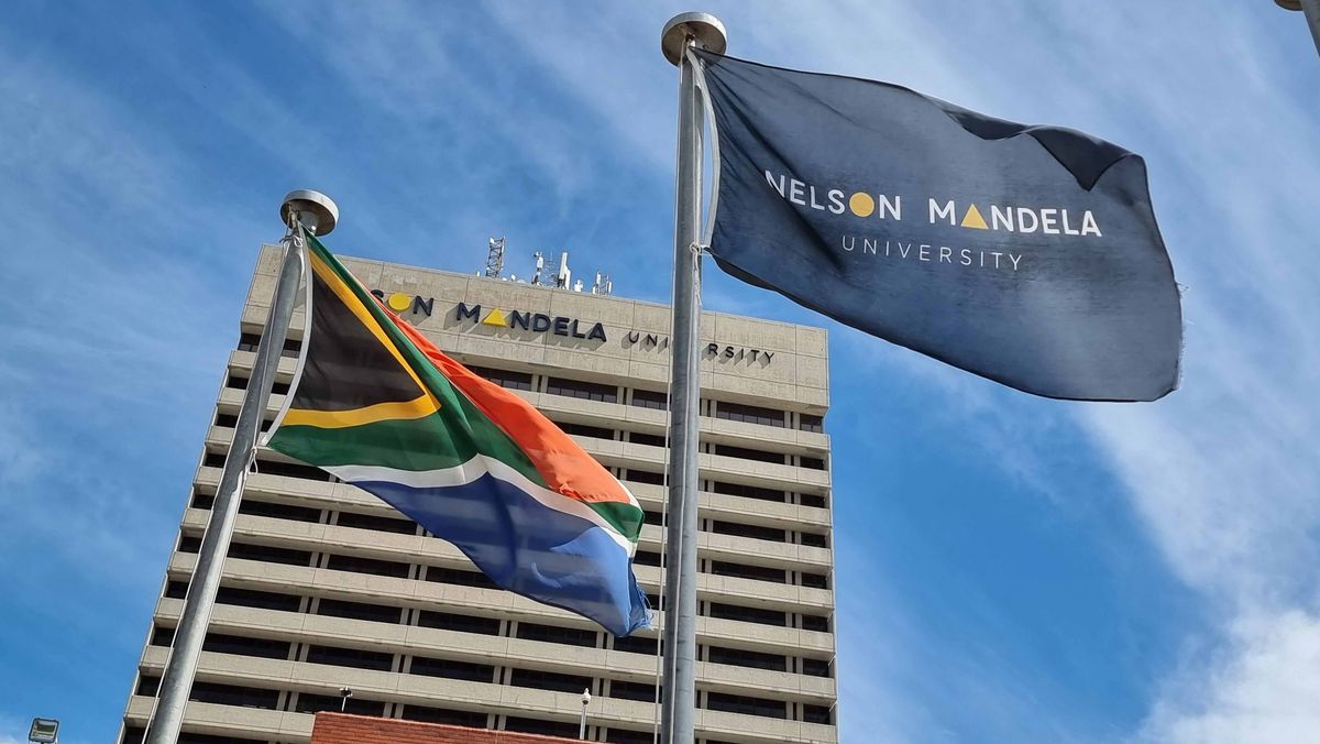 Nelson Mandela Unviersity Flaggen der Nelson Mandela University und Südafrikas wehen im Wind vor einem hohen Gebäude.
