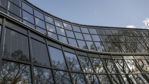 Auf den Scheiben der Glasfassade spiegeln sich der blaue Himmel, die Bäume und einige Wolken.. 
