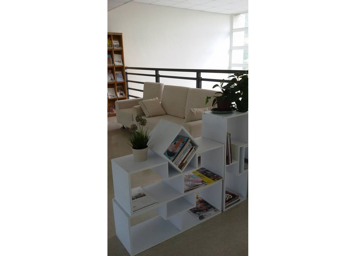 Das Bild zeigt einen minimalistisch eingerichteten Innenraum mit einem weißen Regal, einem beigen Sofa und Pflanzen, der eine einladende und ruhige Atmosphäre schafft.