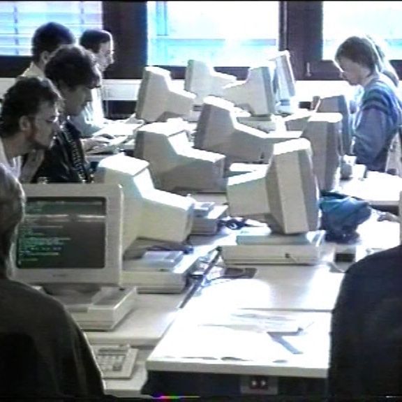 Das Bild zeigt junge Menschen, die an Röhrenmonitoren sitzen und arbeiten.