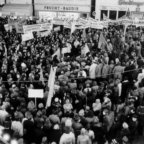 Das Bild zeigt eine Demonstration in der Innenstadt von Oldenburg in den frühen 1970er Jahren. Mehrere hundert Menschen sind erschienen. Einige halten Plakate hoch, auf denen die Gründung einer Universität beziehungsweise einer Reformuniversität gefordert wird.