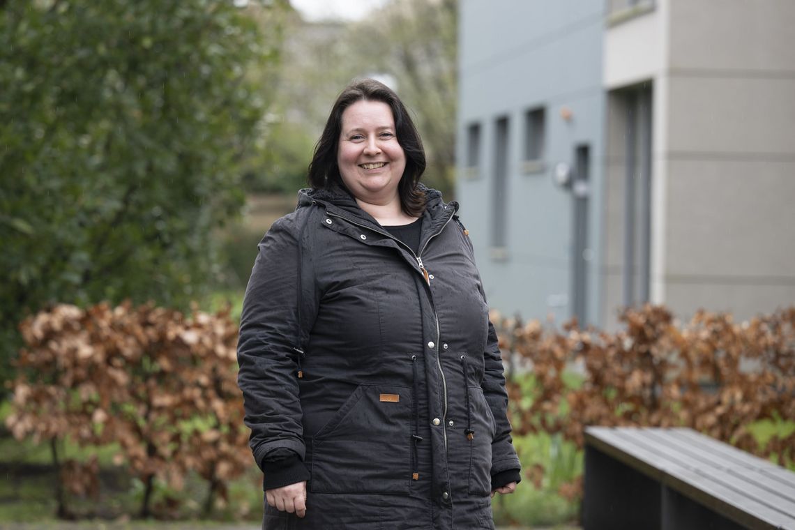 Das Bild zeigt Clara Liehmann. Sie steht hinter dem SSC in einer Regenjacke bei diesigem Wetter. Sie blickt in die Kamera und lächelt dabei.