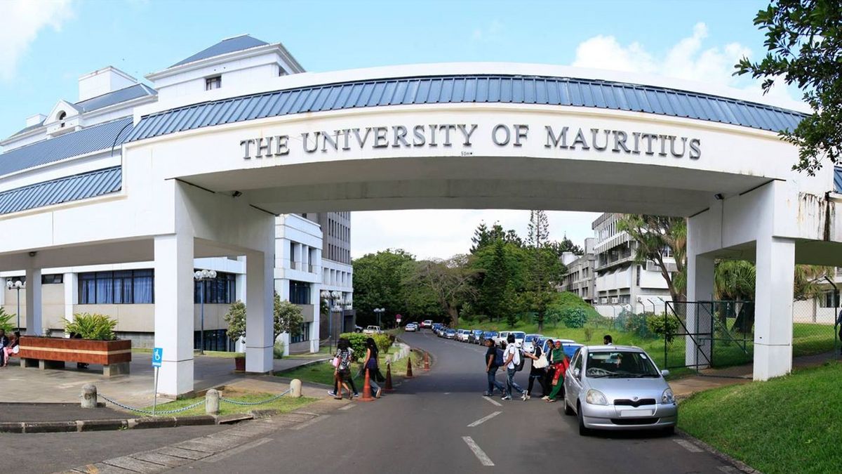 Ein Torbogen mit der Aufschrift "The University of Mauritius" markiert den Eingang zum Campus. Hinter dem Torbogen ist ein Gebäude mit blauer und weißer Fassade zu sehen. Auf dem Campus sind Menschen und Fahrzeuge zu erkennen.