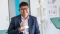 Portrait of Daniel Kristanto. He is wearing glasses and holding a model of a brain. A skeleton stands in the background.