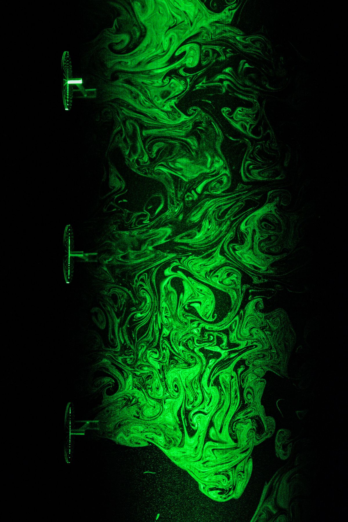 The ordered chaos of turbulence: wind turbines wakes — Gabriele Centurelli — Thousands of wind turbines are going to be installed over the next years just a few Km offshore the German coast as a part of the realization of a carbon-neutral economy by 2050. Our research focuses on understanding how so many wind turbines can coexist in a limited space without dramatically hindering each other performance. As a part of a larger study, a model wind farm was investigated within the wind tunnel of building W33 to study how single turbine wakes merge into a collective wind farm wake. The photo depicts a small portion of the larger wind farm, celebrating the beauty of turbulence and its structures, the main drivers affecting how turbine wakes behave and impact downstream turbines. 