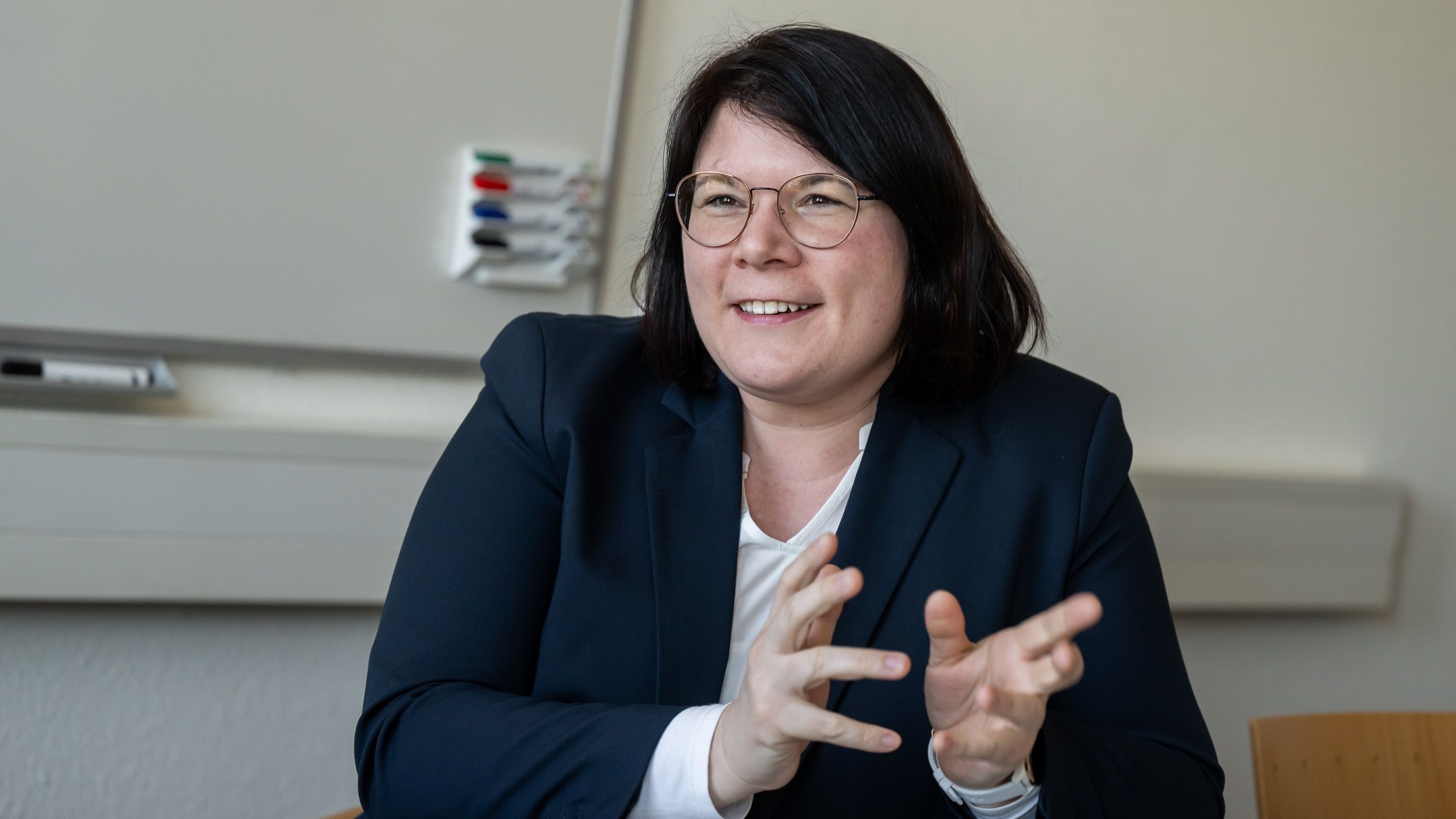 The picture shows Dörte Dannemann. She sits opposite the interviewer and talks. She smiles and gesticulates slightly. A flip chart hangs in the background