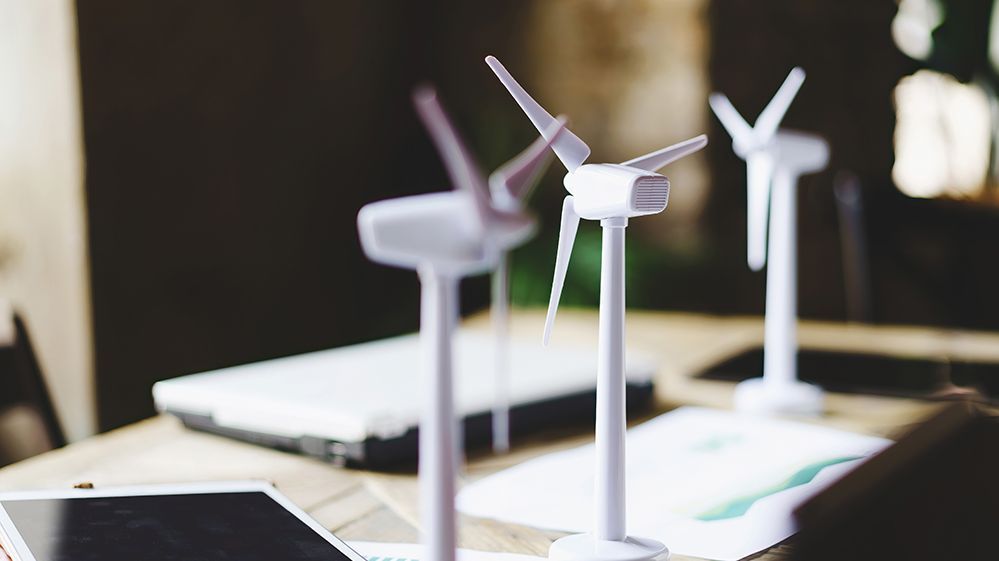 Nahaufnahme von Windkraftanlagen auf einem Tisch mit Datenblättern, Tablet und Laptop