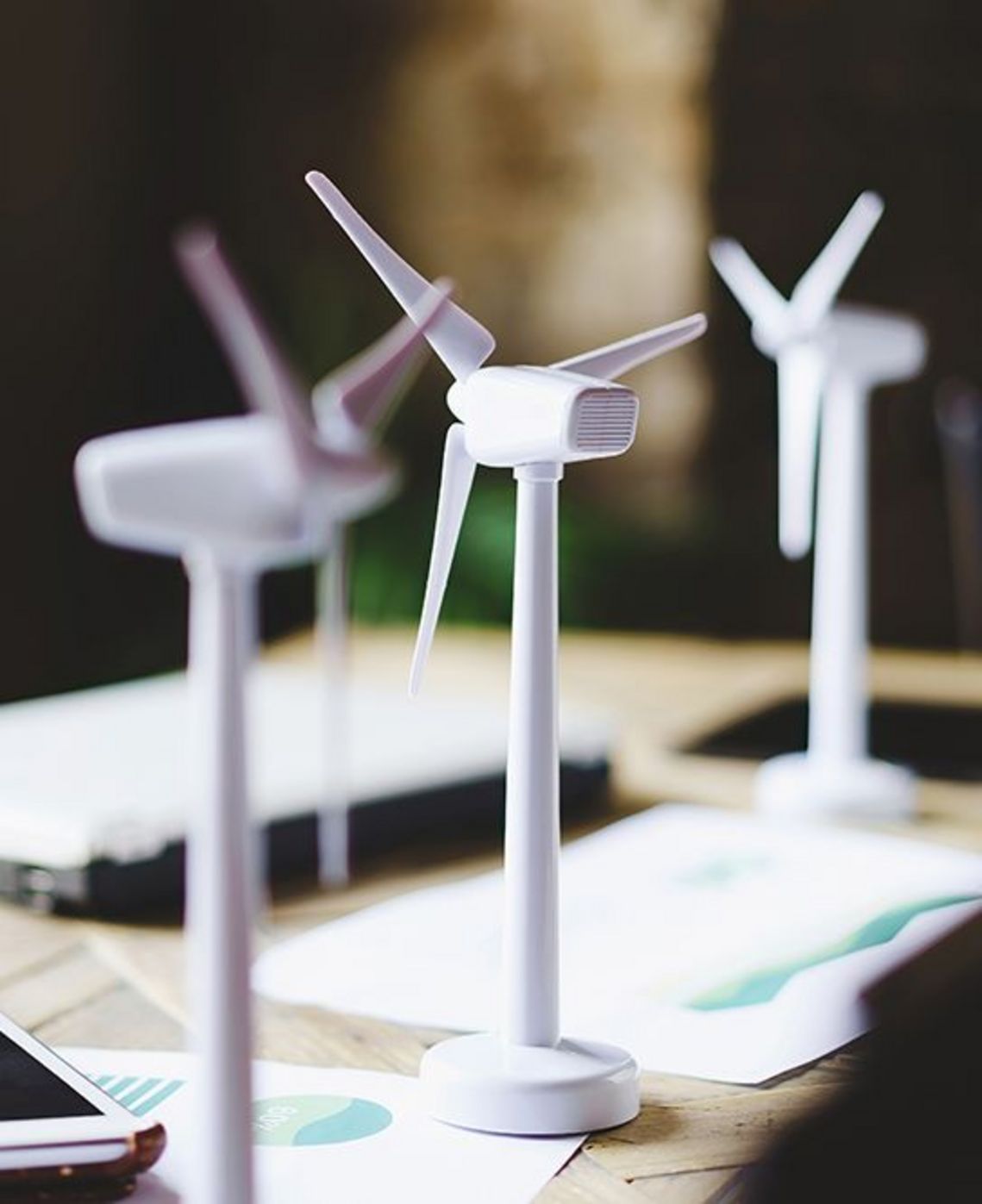 Nahaufnahme von Windkraftanlagen auf einem Tisch mit Datenblättern, Tablet und Laptop